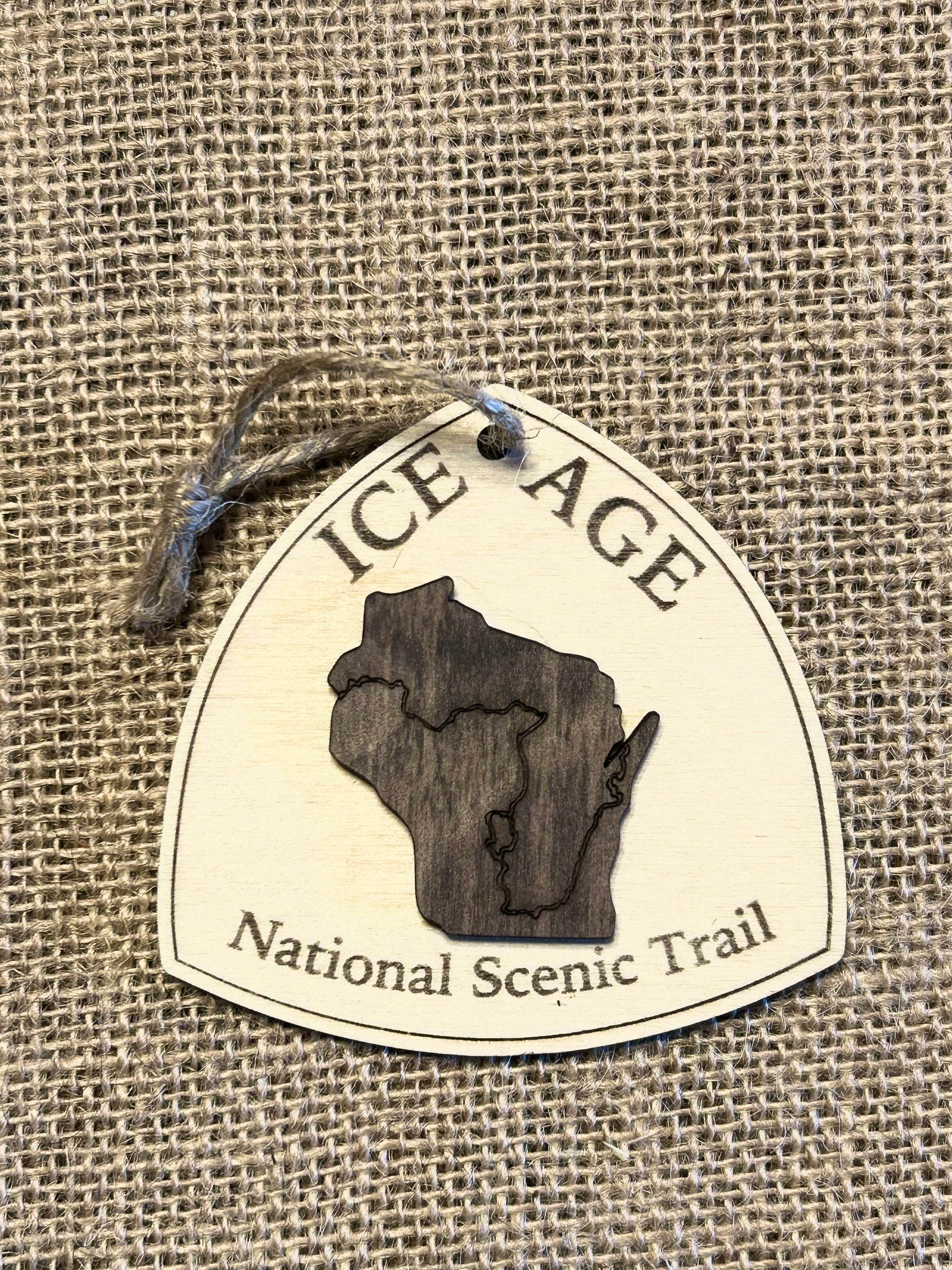 Wood ornament in the shape of the national trail's icon, with a walnut-colored Wisconsin Shaped center piece depicting the Ice Age Trail Route.  Ornament contains the text "Ice Age National Scenic Trail". 