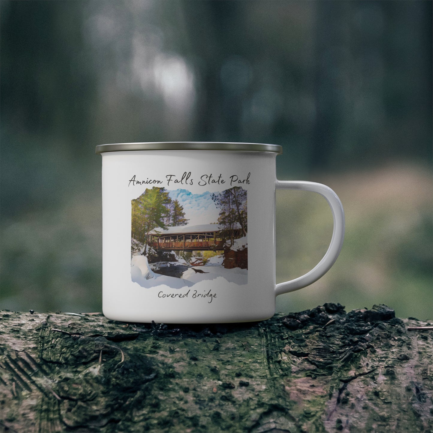 White enamel mug depicting the covered bridge at Amnicon Falls State Park in winter.  Background: mug sitting on a log.