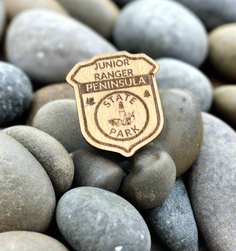 Wood badge shaped junior ranger pin with text Peninsula State Park and a lighthouse icon. 