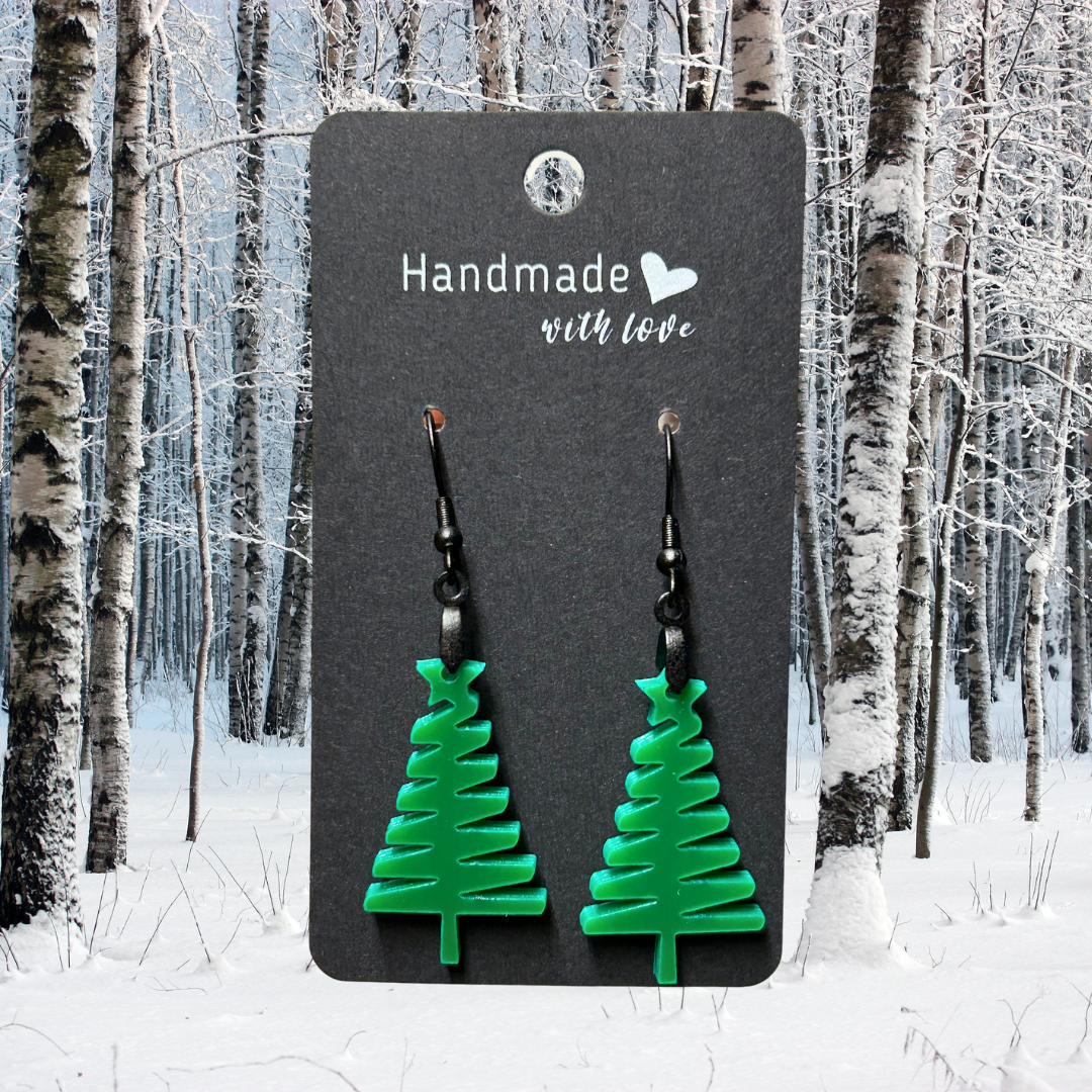 Green acrylic Christmas tree earrings on a black hang tag.  Photo background: snowy woods. 