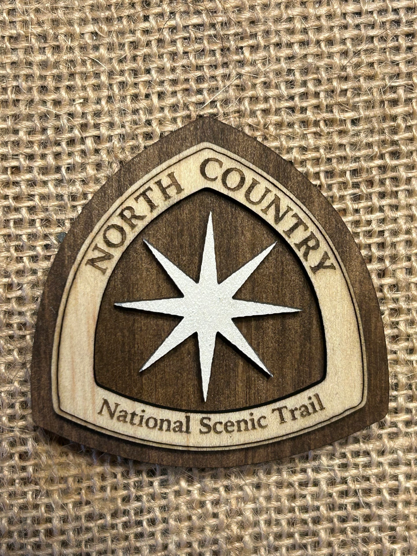 National Trail Icon with Text "North Country National Scenic Trail" and a White Polaris Star Icon on a walnut-colored background. 