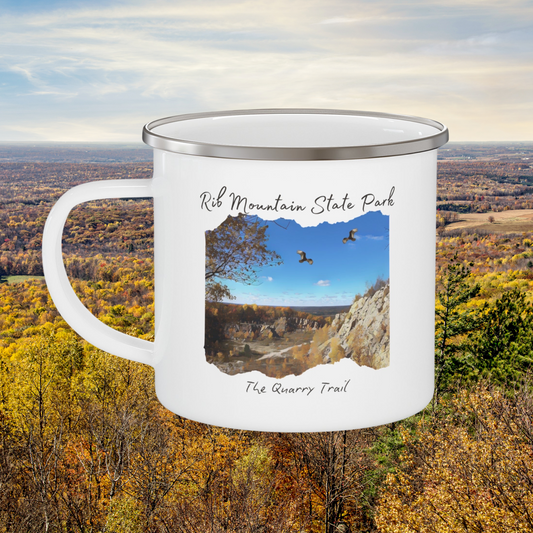 White enamel camper mug with a quarry scene printed on it with the text: Rib Mountain State Park, The Quarry Trail.  Background: countryside in fall leaf color.