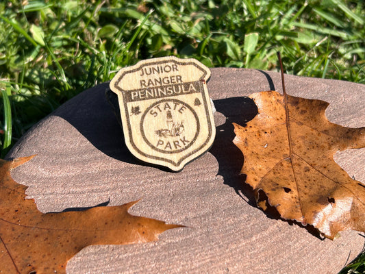 Wood badge shaped junior ranger pin with text Peninsula State Park and a lighthouse icon. 