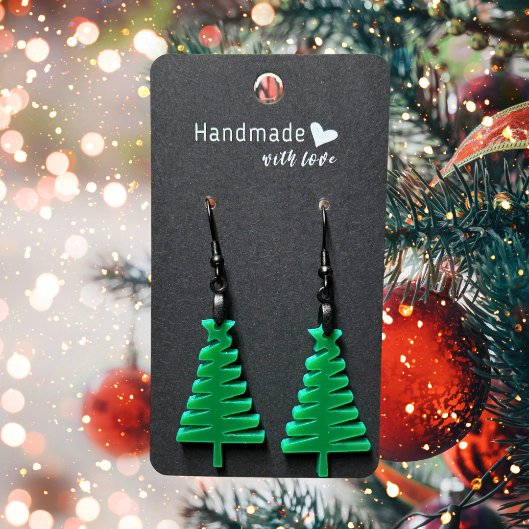 Green acrylic Christmas tree earrings on a black hang tag.  Photo background: Christmas tree and lights. 