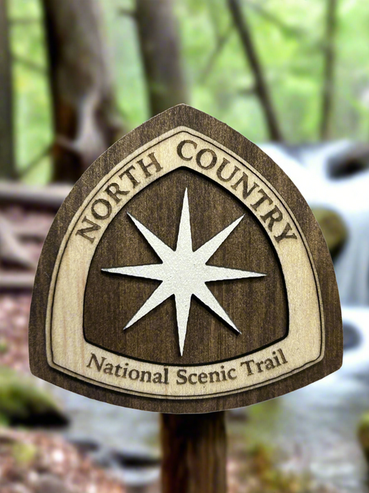 National Trail Icon with Text "North Country National Scenic Trail" and a White Polaris Star Icon on a walnut-colored background. 