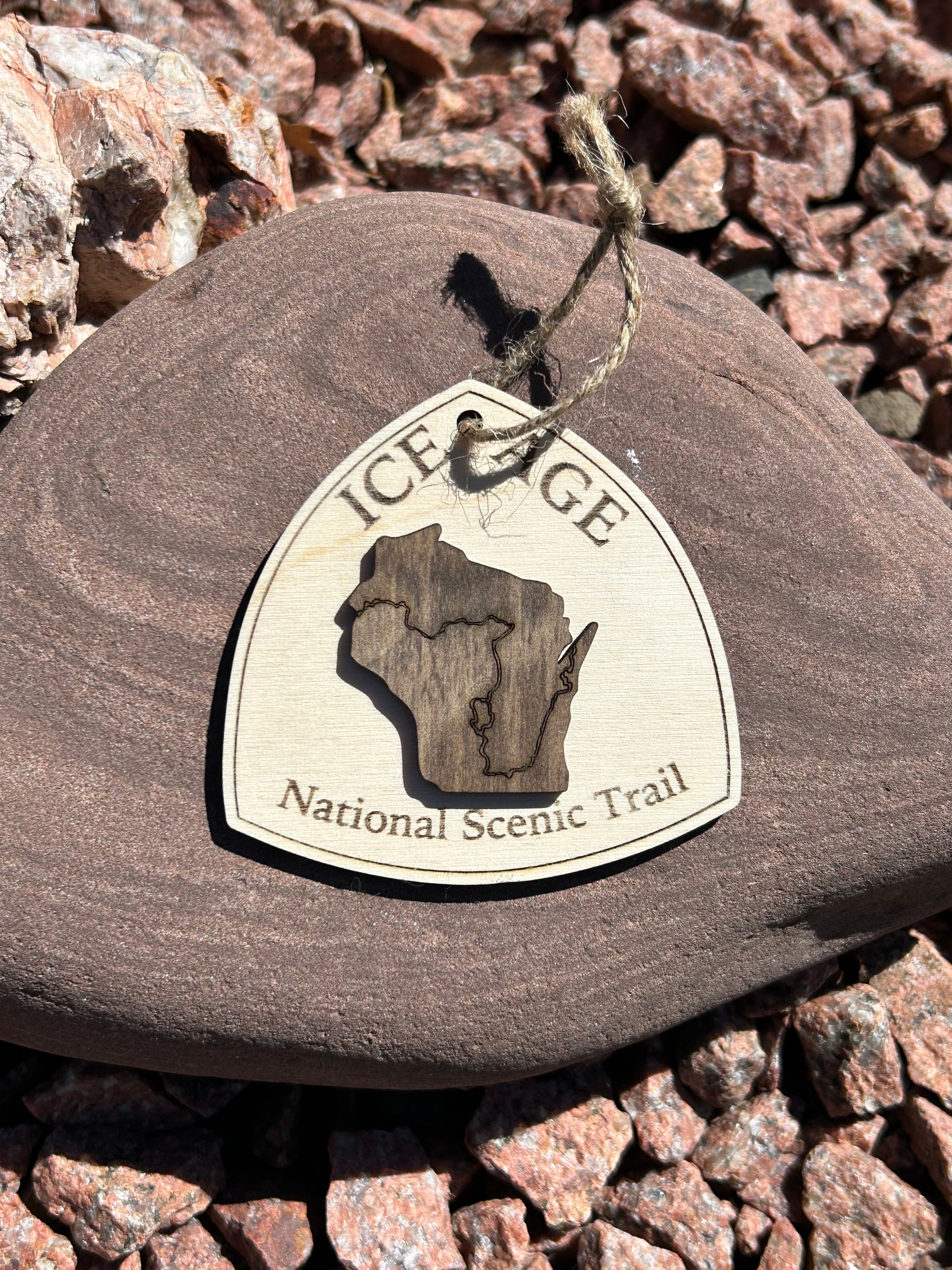 Wood ornament in the shape of the national trail's icon, with a walnut-colored Wisconsin Shaped center piece depicting the Ice Age Trail Route.  Ornament contains the text "Ice Age National Scenic Trail". 