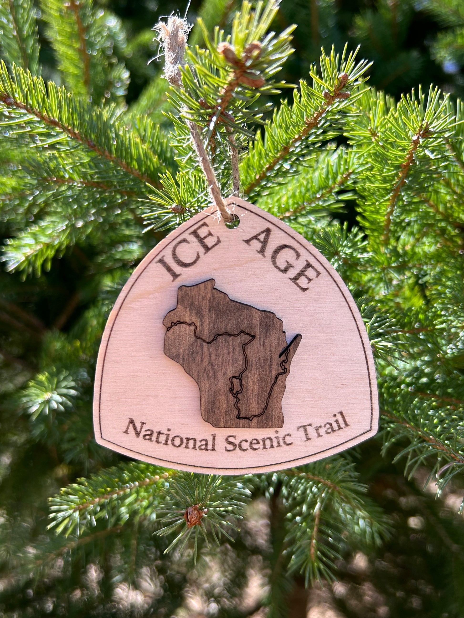 Wood ornament in the shape of the national trail's icon, with a walnut-colored Wisconsin Shaped center piece depicting the Ice Age Trail Route.  Ornament contains the text "Ice Age National Scenic Trail". 