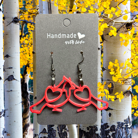 Pair of red cardinal earrings on a black hangtag.  Background of aspen trees and yellow leaves.