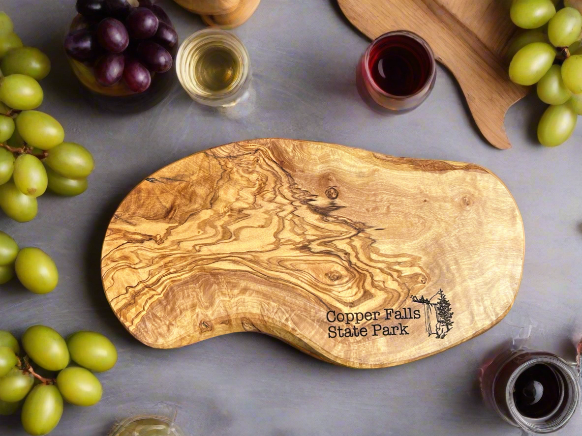 Rustic irregularly shaped olivewood serving board with the Text "Copper Falls State Park" and a waterfall icon. 