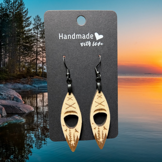 Wood kayak shaped earrings with engraved forest and birds scene.  Photo background: sunset over a calm lake.