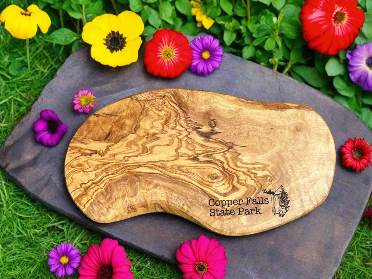 Rustic irregularly shaped olivewood serving board with the Text "Copper Falls State Park" and a waterfall icon. 