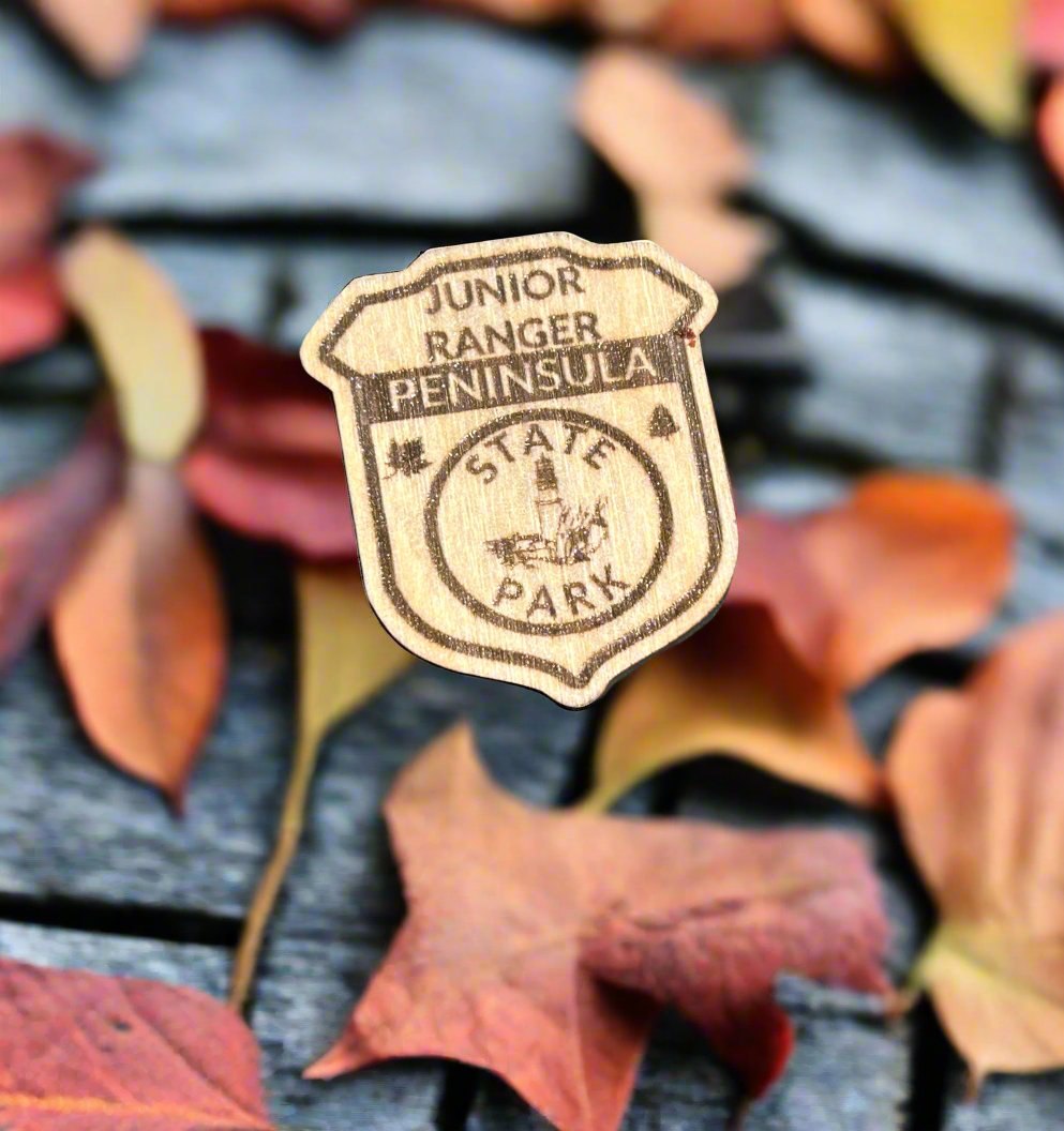 Wood badge shaped junior ranger pin with text Peninsula State Park and a lighthouse icon. 